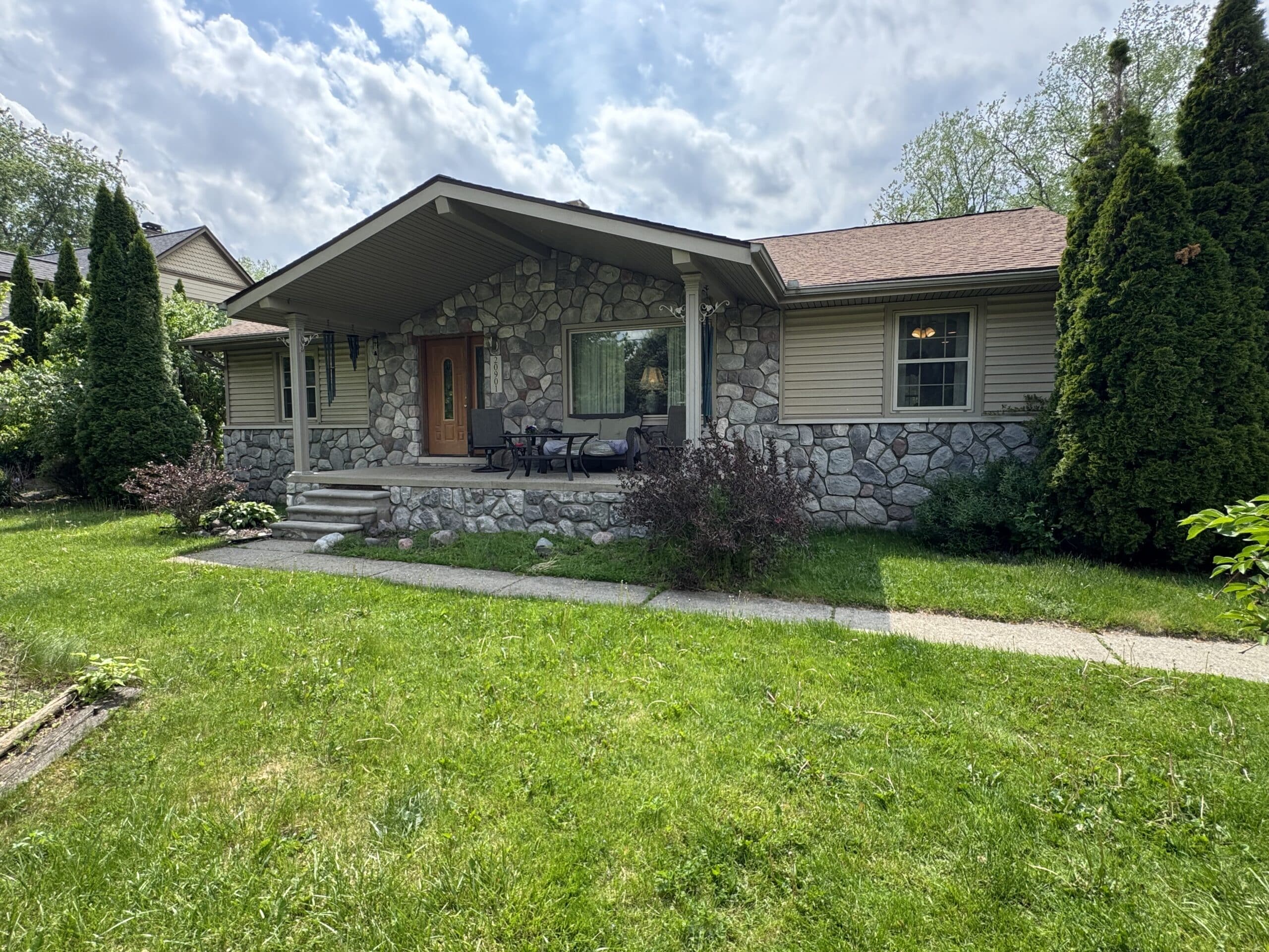 Stone and siding ranch home with a front lawn and evergreen shrubs