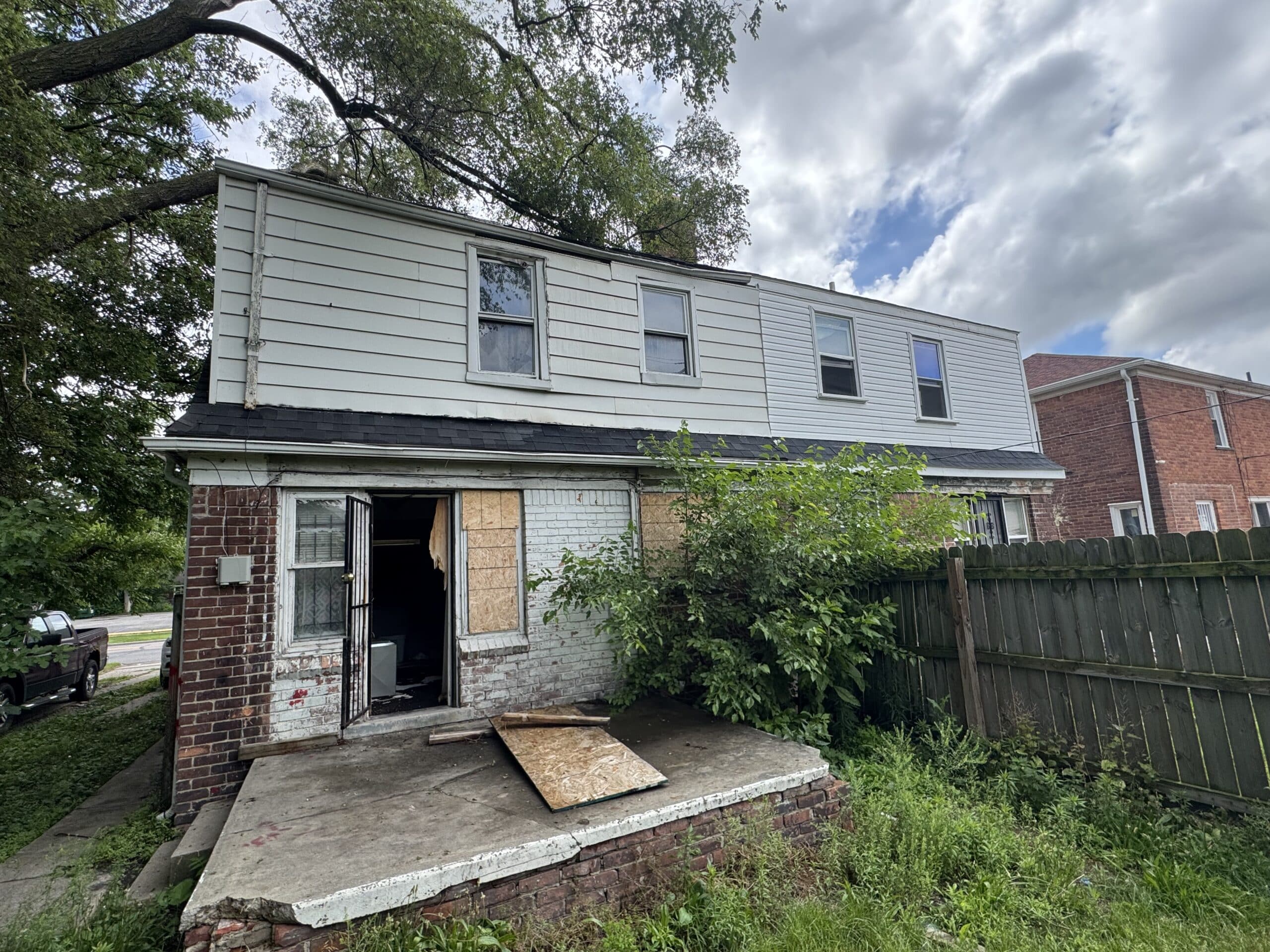 Two story house with damaged siding and an open doorway in Mason