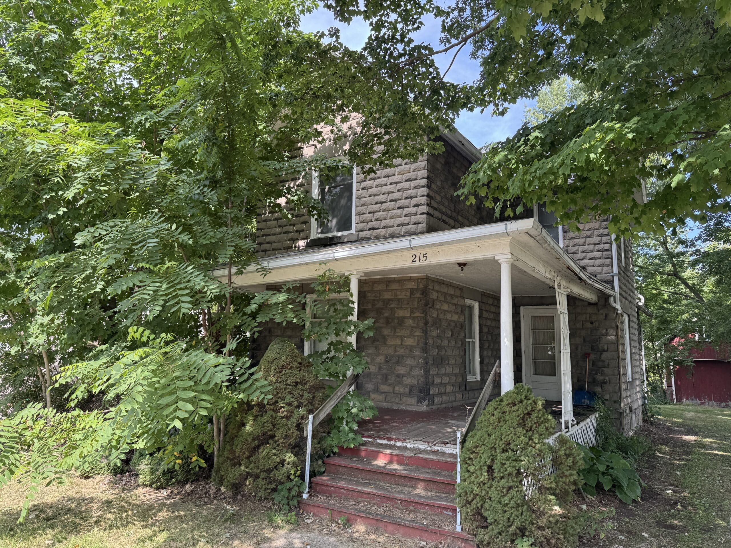 Stone house with a covered porch surrounded by shade trees in Okemos